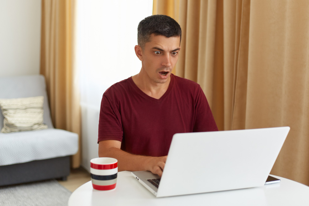 indoor-shot-of-astonished-male-freelancer-working-online-looking-at-notebook-display-with-widely-opened-mouth-having-system-error-being-scared-to-loose-done-work