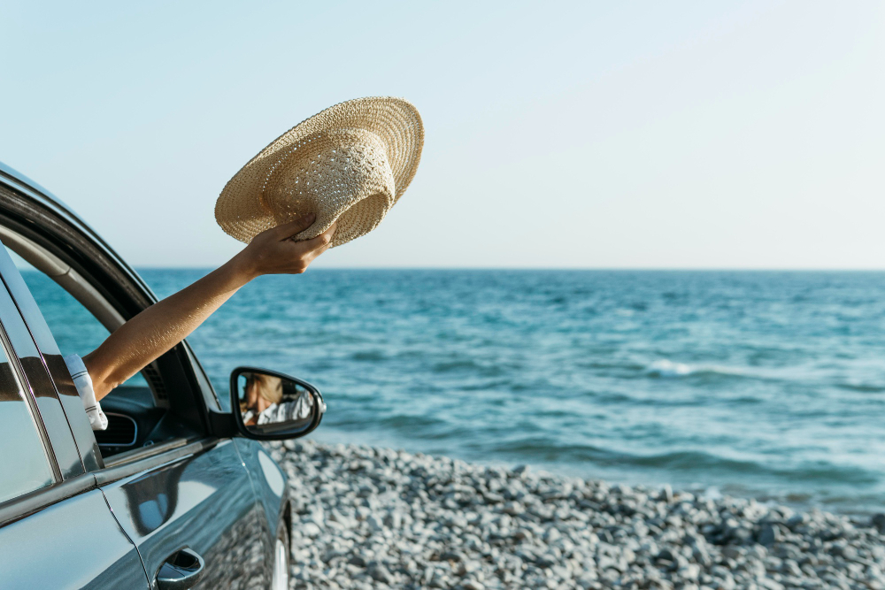 mid-shot-woman-hand-out-of-car-window-and-holding-hat-near-sea