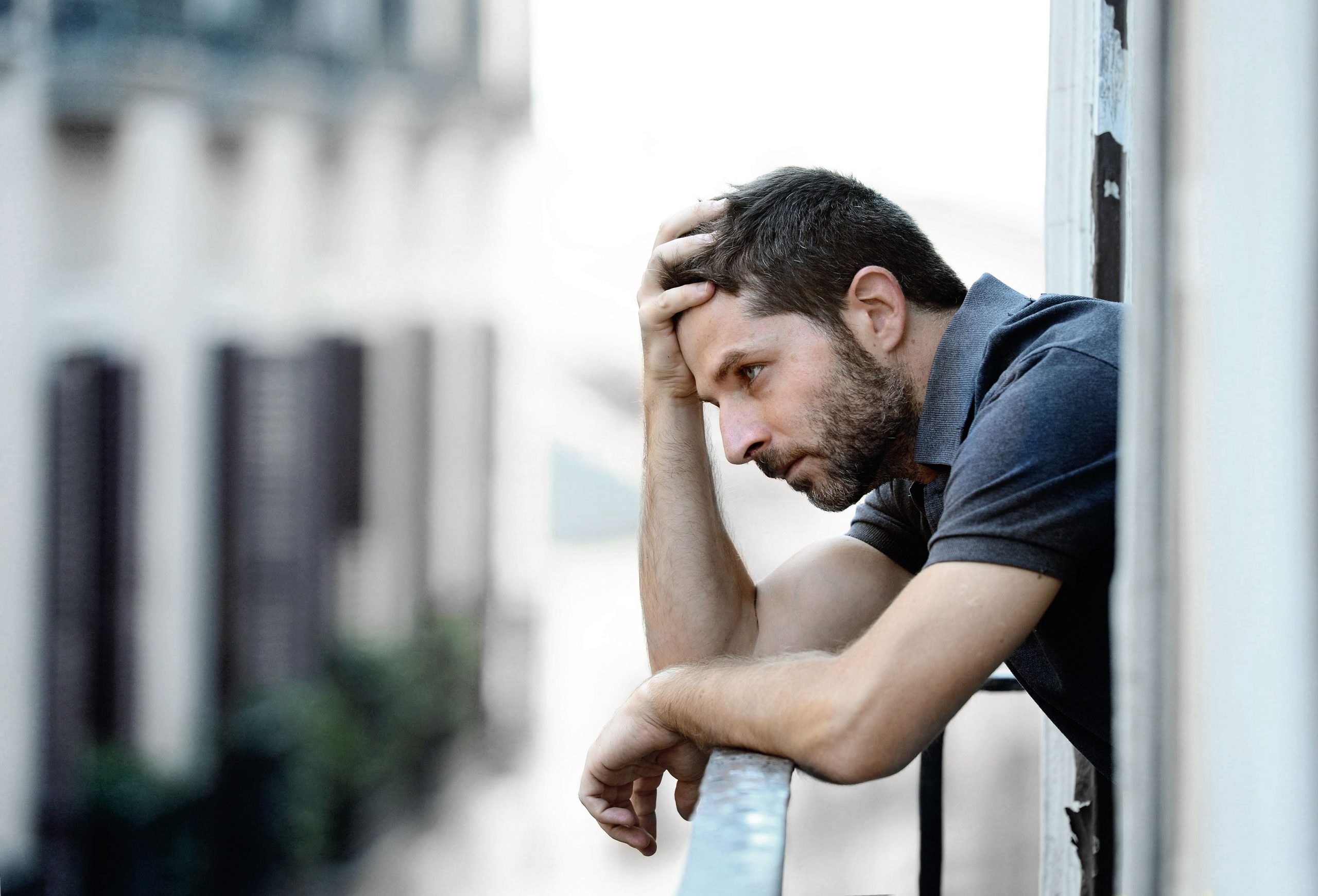 Lonely young man outside at house balcony looking depressed destroyed sad and suffering emotional crisis and grief on an urban background