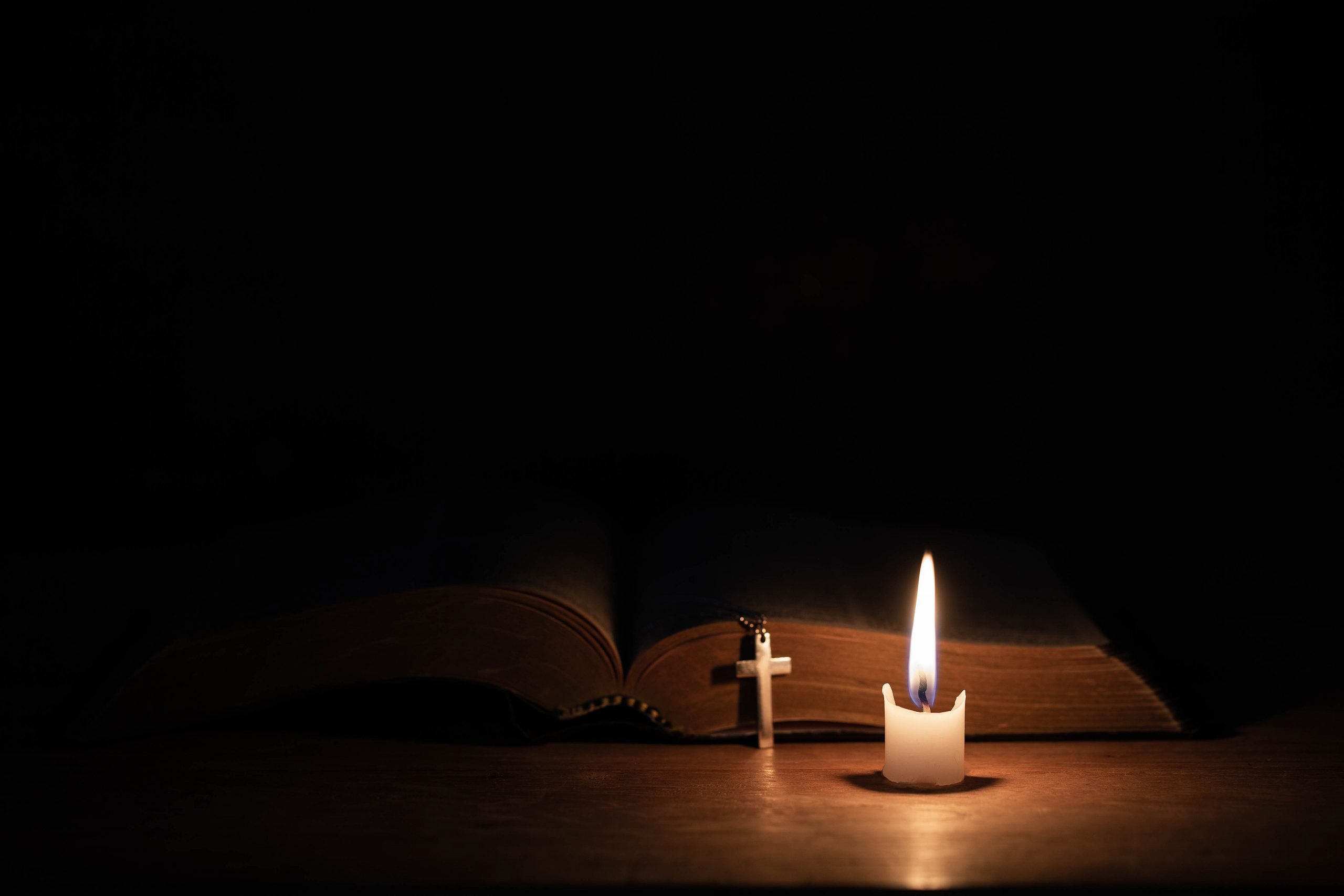 Cross with bible and candle on a old oak wooden table. Beautiful gold background. Religion concept.