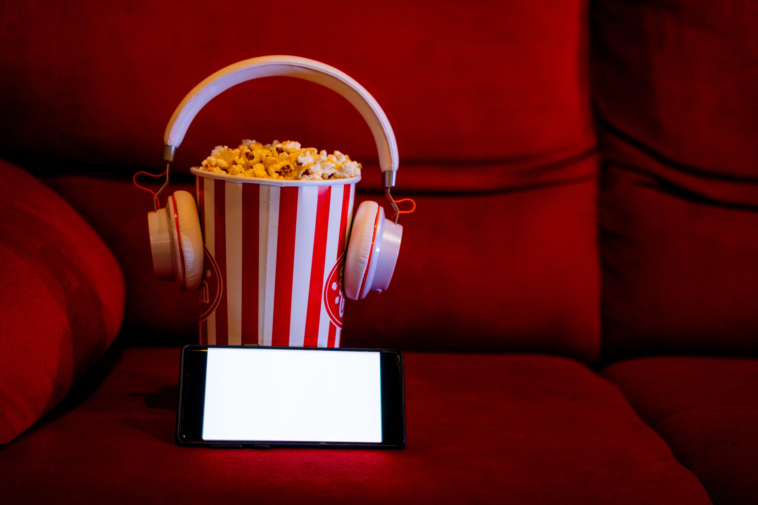 mobile phone with empty white bright screen with popcorn bucket on the red sofa. Concept of streaming TV on internet phone.
