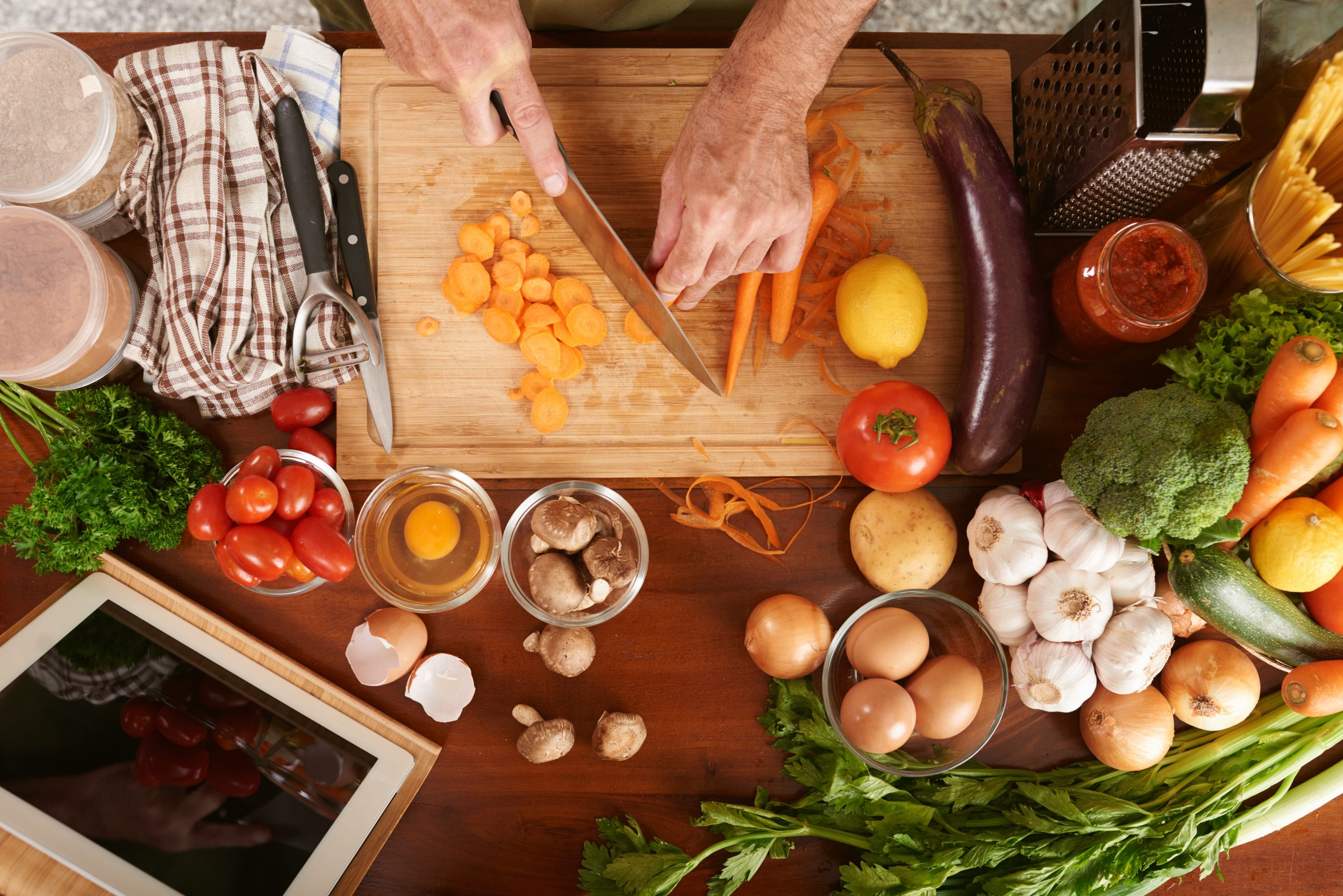Male cook cutting carrots into rounds, there are various fresh vegetables on his table