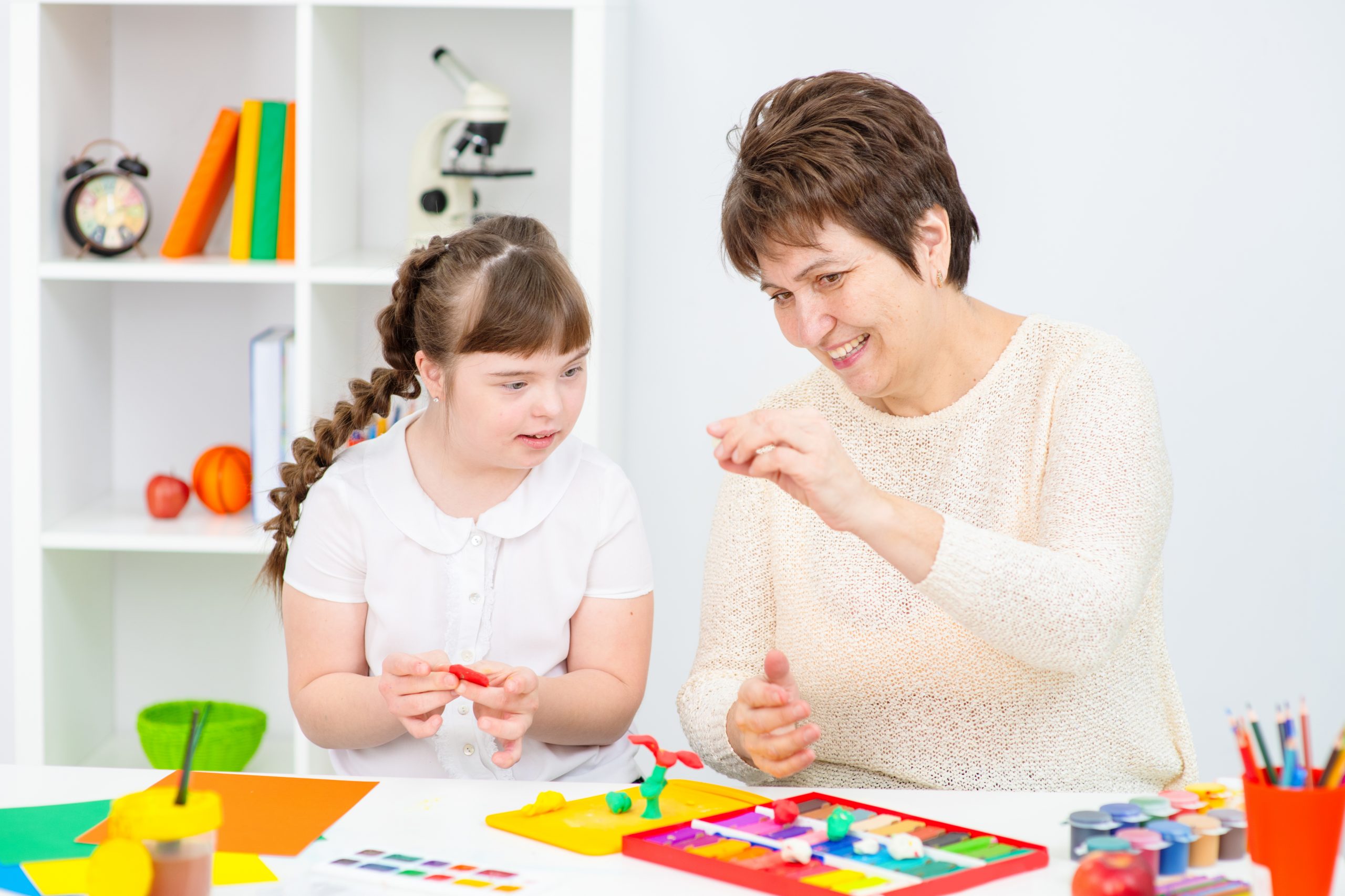 The teacher shows the student with down syndrome how to do creativity. Girl with down syndrome smiles at teacher
