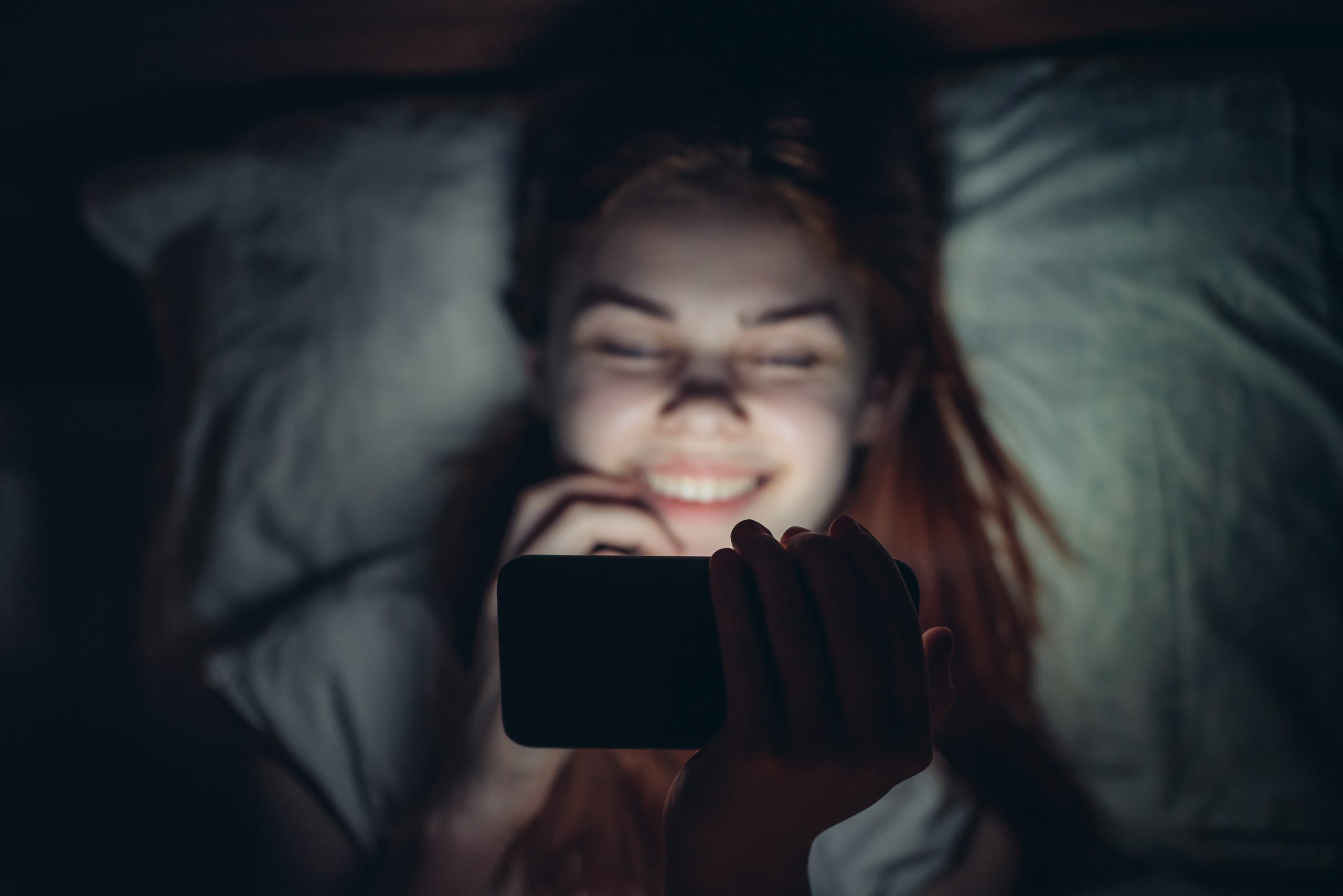 pretty woman lies in bed with a phone in her hands at night addiction relaxation. High quality photo