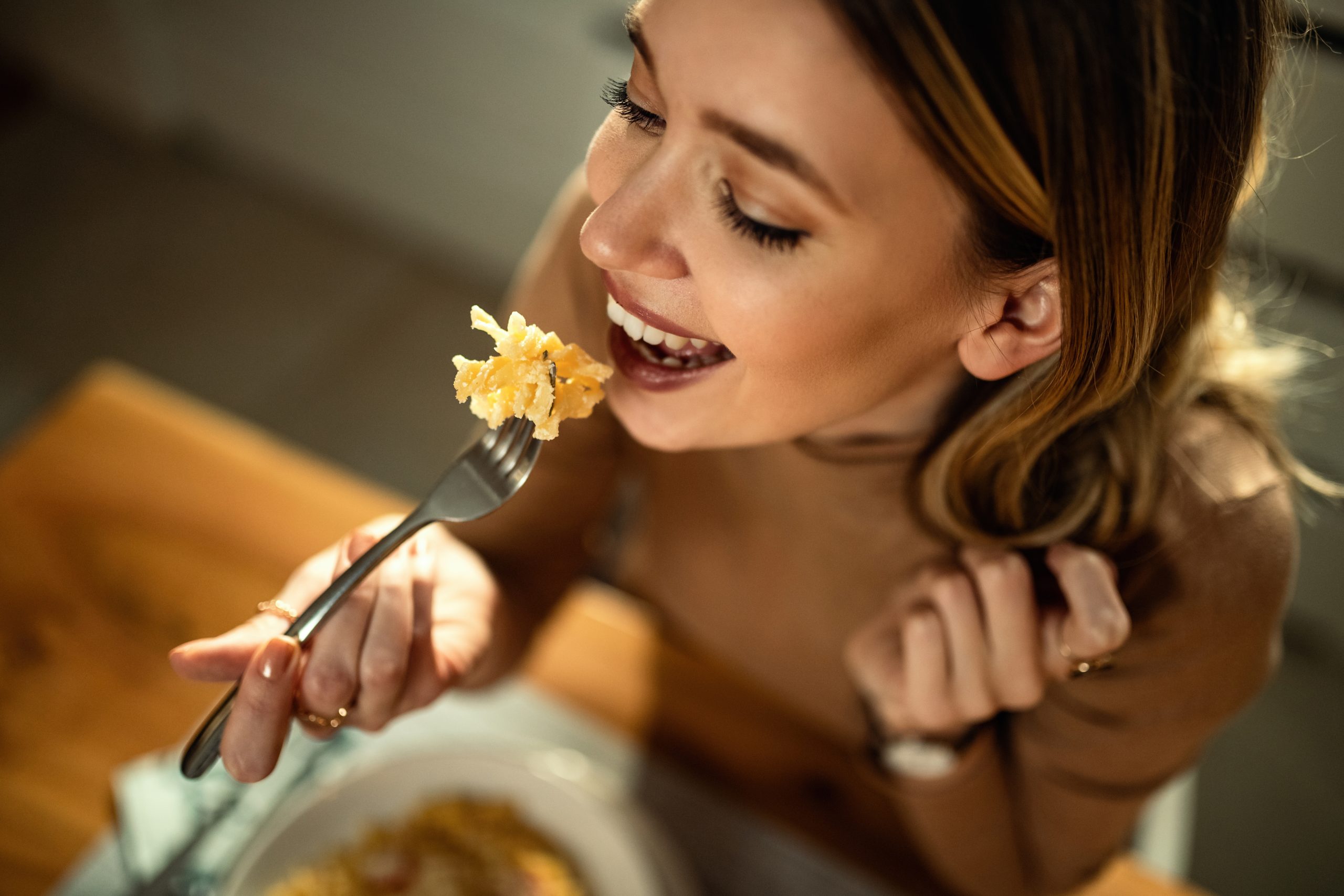 Close-up of young happy woman eating pasta at dining table.