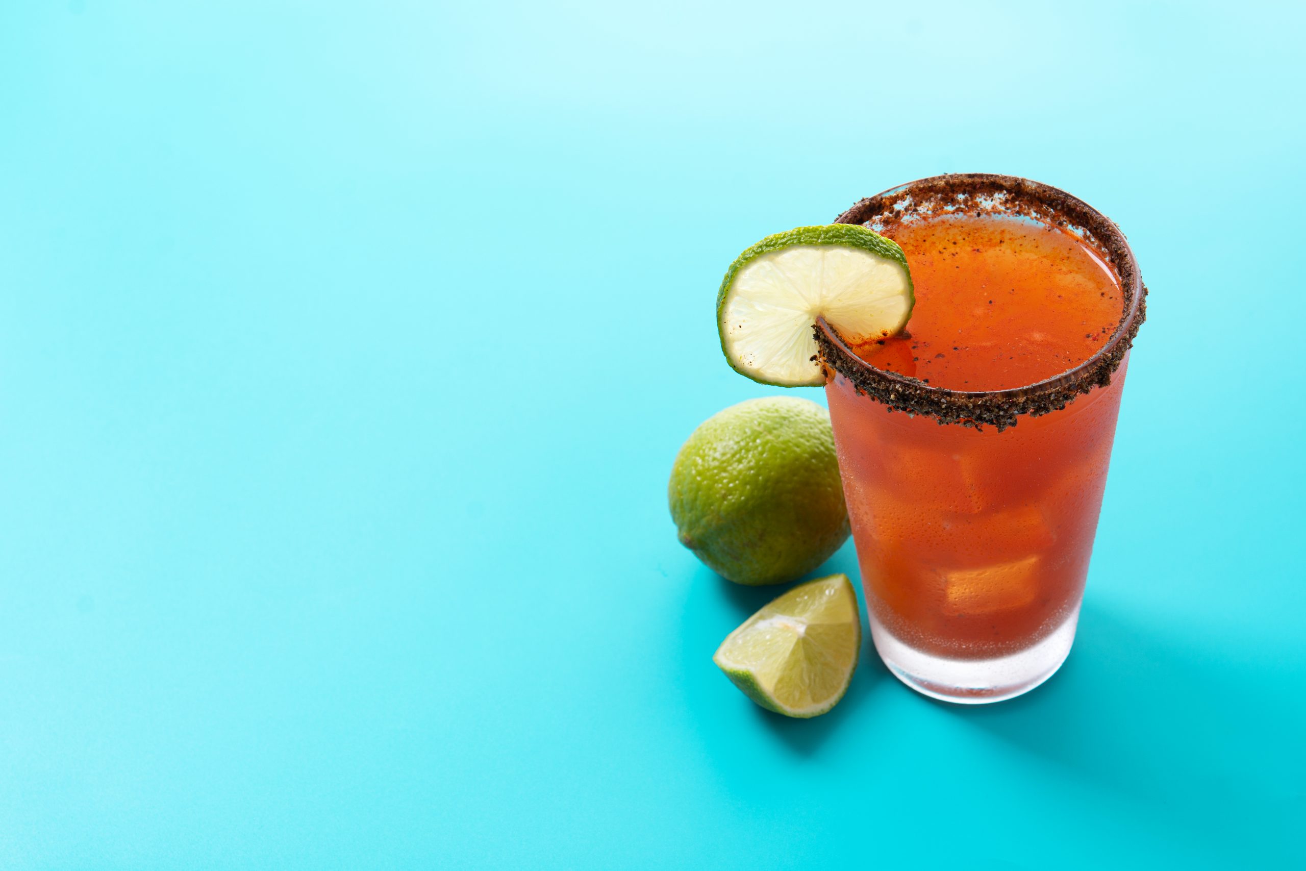 Homemade michelada cocktail with beer, lime juice,hot sauce,salted rim and tomato juice on blue background