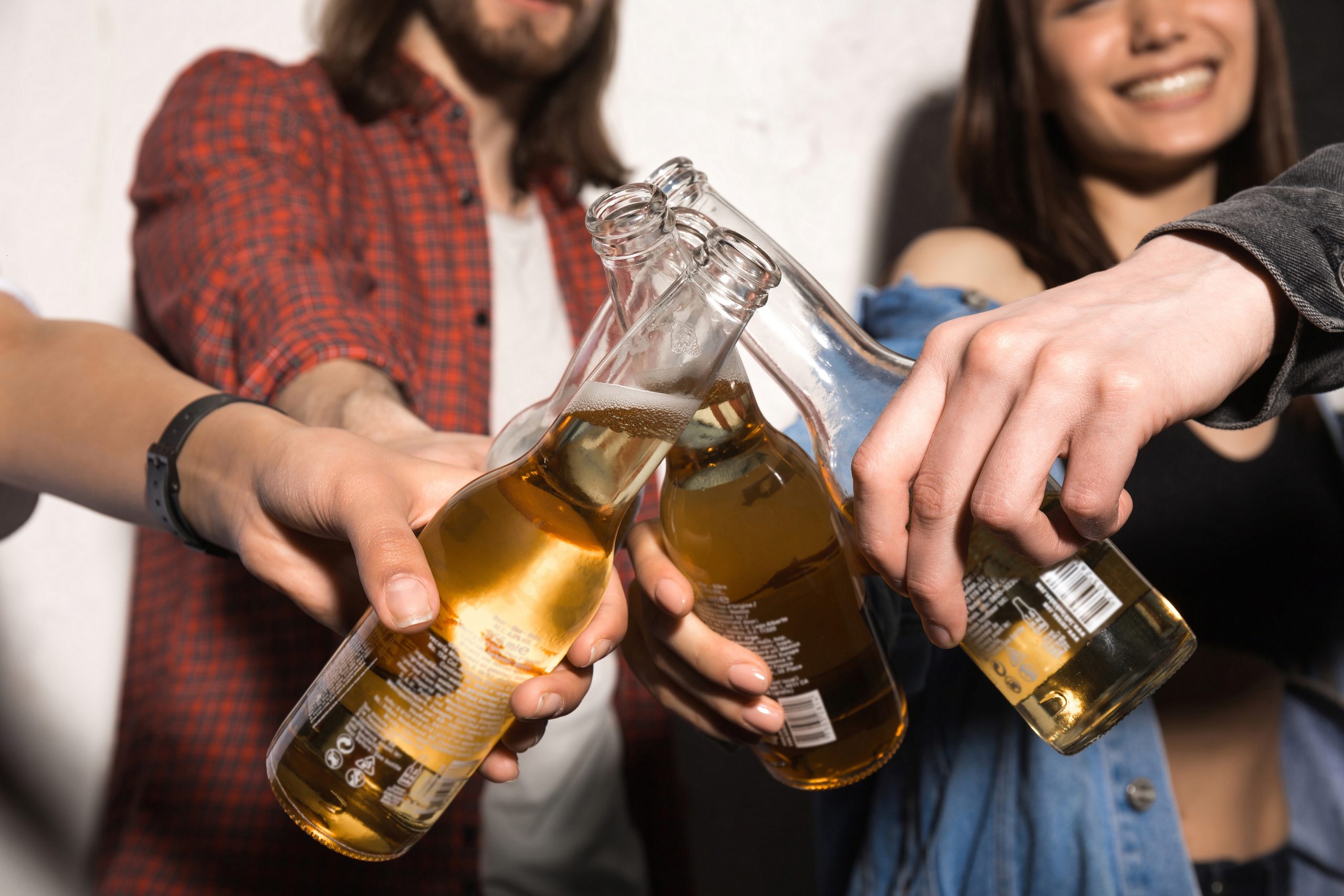 Cropped picture of young hipsters friends standing over gray background drinking beer.