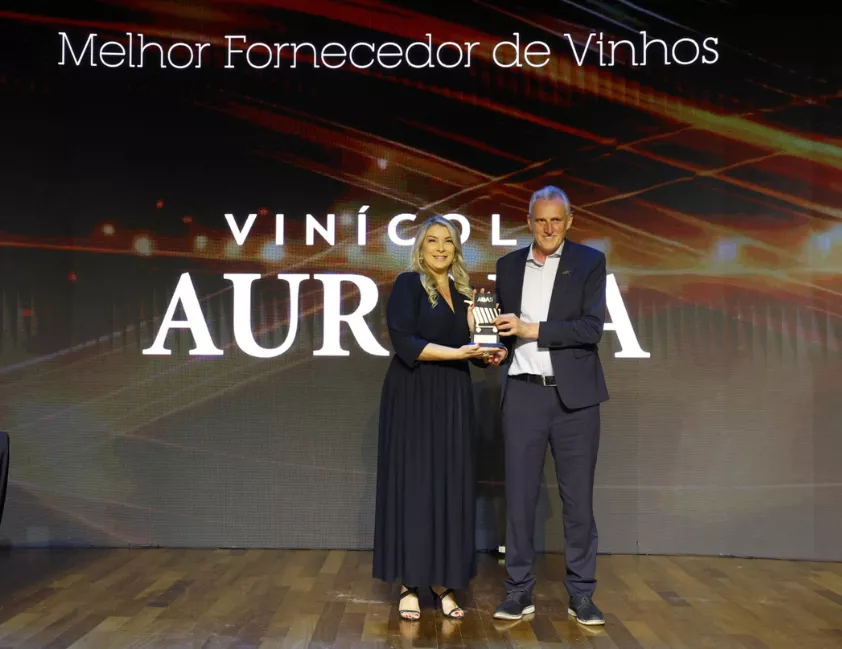 gerente Comercial Regional Sul da Cooperativa Vinícola Aurora, Rejane Farias, recebeu o troféu de Melhor Fornecedora de Vinhos no Carrinho AGAS 2025 das mãos do diretor da entidade, Paulo Bruschi